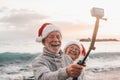 Portrait of two cute old persons having fun and enjoying together at the beach on christmas days at the beach wearing Christmas Royalty Free Stock Photo