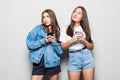 Portrait of two cute women phone addicted friends isolated over gray background Royalty Free Stock Photo