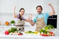 Portrait of two delighted overjoyed partners raise fists up celebrate success achieve kitchen indoors