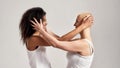 Portrait of two diverse women touching hair while standing opposite each other isolated over grey background. Diversity Royalty Free Stock Photo