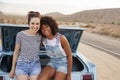 Portrait Of Two Female Friends Sitting In Trunk Of Classic Car On Road Trip Royalty Free Stock Photo