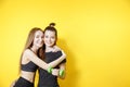 Portrait of two fitness females on yellow background. Young women friends standing against wall and smiling