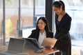 Two friendly businesswomen using laptop computer and working on project together in modern office. Royalty Free Stock Photo