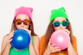 Portrait of two girls in hats and spectacles blowing balloons Royalty Free Stock Photo