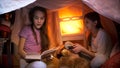 Portrait of two girls reading fairy tales in tent made of blankets at home