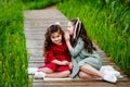 Portrait of two girls in a red and green dress, smiling outdoors, enjoying a warm sunny summer day. The sisters are sitting on a Royalty Free Stock Photo