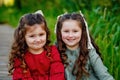 Portrait of two girls in a red and green dress, smiling outdoors, enjoying a warm sunny summer day. The sisters are sitting on a Royalty Free Stock Photo