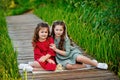 Portrait of two girls in a red and green dress, smiling outdoors, enjoying a warm sunny summer day. The sisters are sitting on a Royalty Free Stock Photo