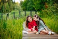 Portrait of two girls in a red and green dress, smiling outdoors, enjoying a warm sunny summer day. The sisters are sitting on a Royalty Free Stock Photo