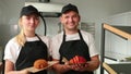 Portrait of two good looking young smiled male female bakers posing, croissants