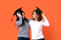 Happy mixed-race women graduating holding there graduation caps looking at each other in orange  studio Royalty Free Stock Photo