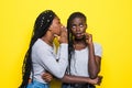 Portrait of two happy young african women sharing secrets isolated over yellow background Royalty Free Stock Photo