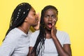 Portrait of two happy young african women sharing secrets isolated over yellow background Royalty Free Stock Photo