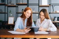 Portrait of two happy young business women working using digital tablet at meeting desk with job documents at office. Royalty Free Stock Photo