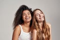 Portrait of two happy young diverse women in white shirts smiling at camera while posing together isolated over grey Royalty Free Stock Photo