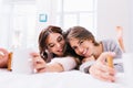 Portrait two joyful smiling young women chilling on bed with cups of tea. Waking up in the morning in modern apartment