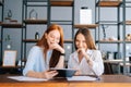 Portrait of two laughing young business women working using digital tablet at meeting desk with job documents at office. Royalty Free Stock Photo