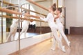 Portrait of two little ballerinas in white ballet leotards doing gymnastics standing by bar in ballet studio