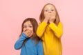 Portrait of two little frightened girls covering mouth with hands and looking with scared eyes
