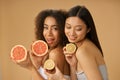 Portrait of two lovely mixed race young women holding grapefruit and lemon cut in half while posing isolated over beige Royalty Free Stock Photo