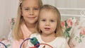 Portrait of two lovely sisters sitting on a bed with a toy