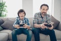 Portrait of two nice attractive cheerful cheery guys dad and pre-teen son sitting on sofa playing online video game Royalty Free Stock Photo