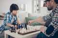Portrait of two nice skilled focused serious guys dad and pre-teen son sitting on sofa playing chess moving pieces