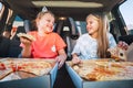 Portrait of two positive smiling sisters eating Huge just cooked italian pizzas sitting in child car seats on car back seat. Happy Royalty Free Stock Photo