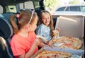 Portrait of two positive smiling sisters eating just cooked italian pizza sitting in child car seats on car back seat. Happy Royalty Free Stock Photo