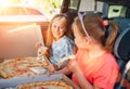 Portrait of two positive smiling sisters eating just cooked italian pizza sitting in child car seats on car back seat. Happy Royalty Free Stock Photo