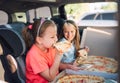 Portrait of two positive smiling sisters eating just cooked italian pizza sitting in child car seats on car back seat. Happy Royalty Free Stock Photo