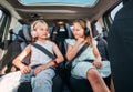 Portrait of two positive smiling sisters sitting in child car seats fastening safety belts listening to music using headphones. Royalty Free Stock Photo