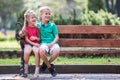 Portrait of two pretty cute children boy and girl having fun time on a bench in summer park outdoors Royalty Free Stock Photo