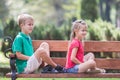 Portrait of two pretty cute children boy and girl having fun time on a bench in summer park outdoors Royalty Free Stock Photo