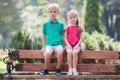 Portrait of two pretty cute children boy and girl having fun time on a bench in summer park outdoors Royalty Free Stock Photo