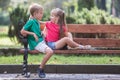 Portrait of two pretty cute children boy and girl having fun time on a bench in summer park outdoors Royalty Free Stock Photo