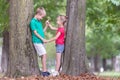 Portrait of two pretty cute children boy and girl standing near big tree trunk in summer park outdoors Royalty Free Stock Photo