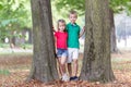 Portrait of two pretty cute children boy and girl standing near big tree trunk in summer park outdoors Royalty Free Stock Photo