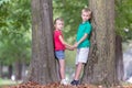 Portrait of two pretty cute children boy and girl standing near big tree trunk in summer park outdoors Royalty Free Stock Photo