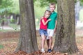 Portrait of two pretty cute children boy and girl standing near big tree trunk in summer park outdoors Royalty Free Stock Photo