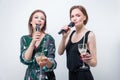 Portrait of two singing girls with glasses in their hands. Karaoke concept