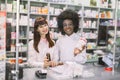 Portrait of two smiling friendly multiethnic female pharmacists working in modern farmacy, posing at the counter