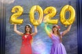 Portrait of two smiling happy girls in christmas dresses posing with gold colored number balloons 2020