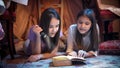 Closeup portrait of two teenage girls with flashlight lying on floor and reading scary book Royalty Free Stock Photo