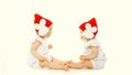 Portrait of two twin babies looking at each other wearing red winter knitted hats playing on white background Royalty Free Stock Photo