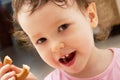 Portrait of a two year old baby girl. The curly child eats a bagel and smiles. Two front teeth are visible. Half-eaten bagel in ha