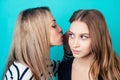 Portrait of two young attractive happy women with blonde hair and makeup eavesdrops whispers a secret mystery in the