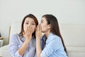 Portrait of two young attractive happy women with eavesdrops whispers a secret mystery in the studio on living room. The