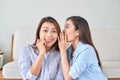 Two happy women with eavesdrops whispers a secret mystery in the studio on living room