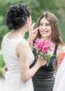 Portrait of two young beautiful women friends. Pretty bride with roses bouquet helping her smiling bridesmaid. Wedding at Sunny su Royalty Free Stock Photo